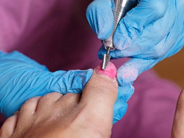 Manicurist applying pink polish to toenail with a rotary tool.