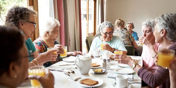 A number of residents are sitting at a table enjoying tea, toast, and orange juice