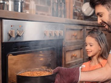 A father and daughter taking a cake/pie out of an oven