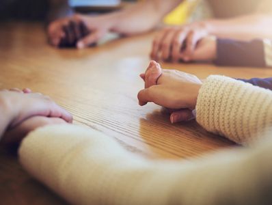 People holding hands around a wooden table, showing unity and support.