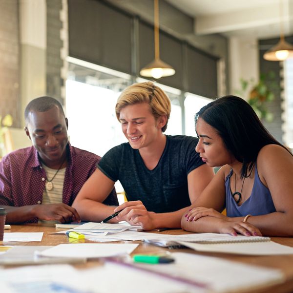 Three students studying together at a table with papers and highlighters.