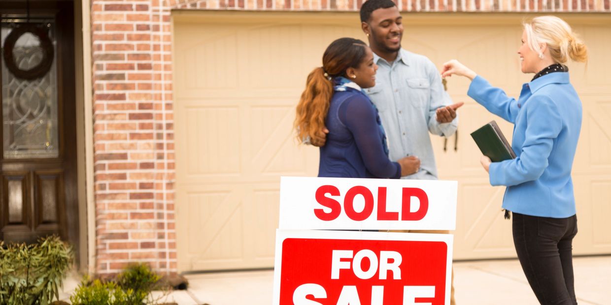 Real estate agent hands keys to happy couple in front of their new house.