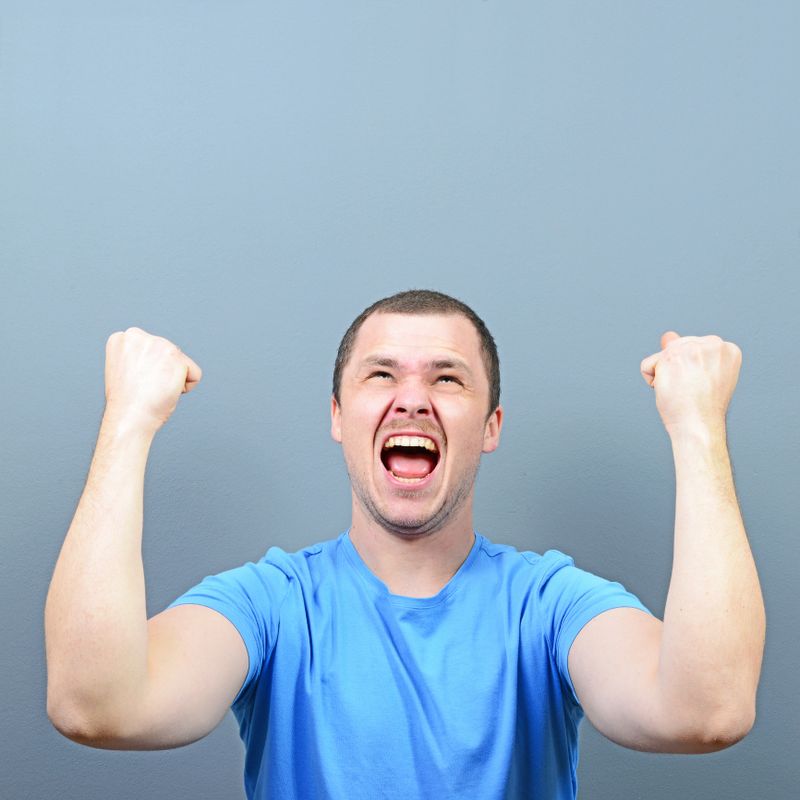 Portrait of ecstatic young man celebrating victory or win against gray background