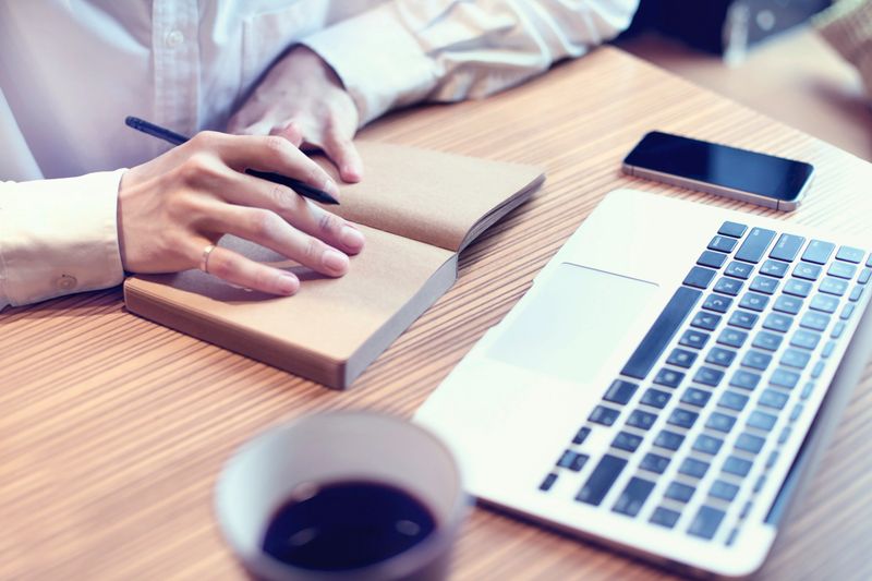 Acounting business man writing business plan, use laptop computer and mobile phone in cafe, drinking coffee.
