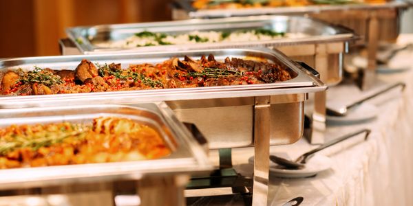 Buffet trays filled with assorted hot dishes and garnished with herbs.