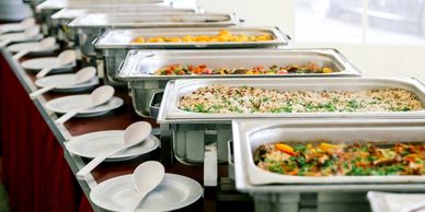 Buffet table with multiple trays of food and serving utensils.