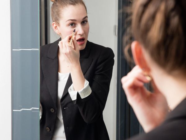 Woman applying makeup in mirror.