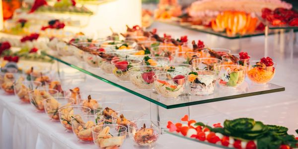 Elegant buffet with assorted appetizers in clear cups arranged on glass shelves.