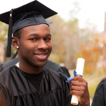 Young man in graduation gown holding diploma and smiling.