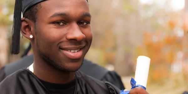 A smiling graduate holding a diploma outdoors.