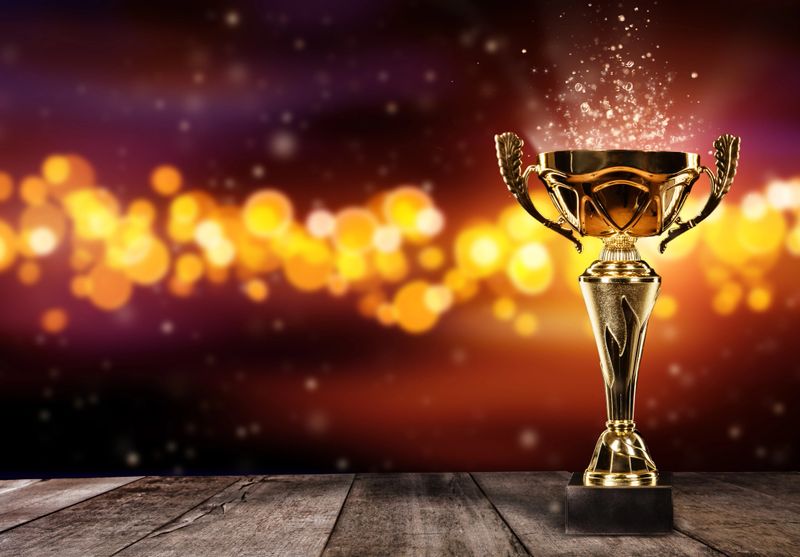 Champion golden trophy on wood table with blur spot lights on background. Copyspace for text, wide banner format. Concept of success and achievement.