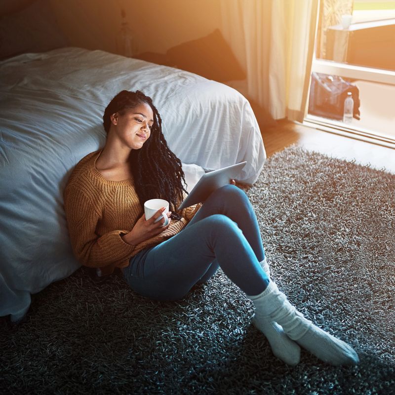 Shot of a relaxed young woman drinking coffee and using a digital tablet at home