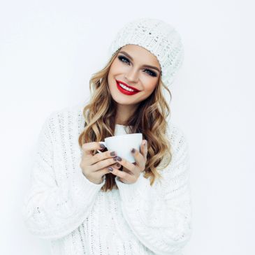 Smiling woman in white knitwear holding a cup.