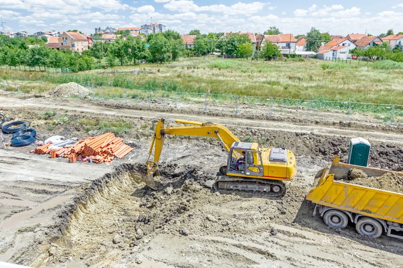 Big excavator is excavating a pit and loading soil into dump truck at construction site, project in progress.