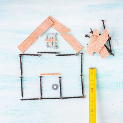 A house shape made from screws and wooden pieces with a measuring tape.