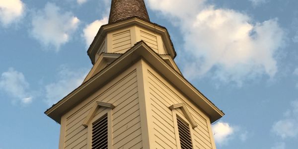 Close-up of a church steeple against a blue sky with clouds.