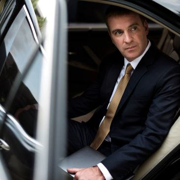 Man in suit sitting in car, holding a tablet.