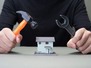 Person holding hammer and wrench over model house.