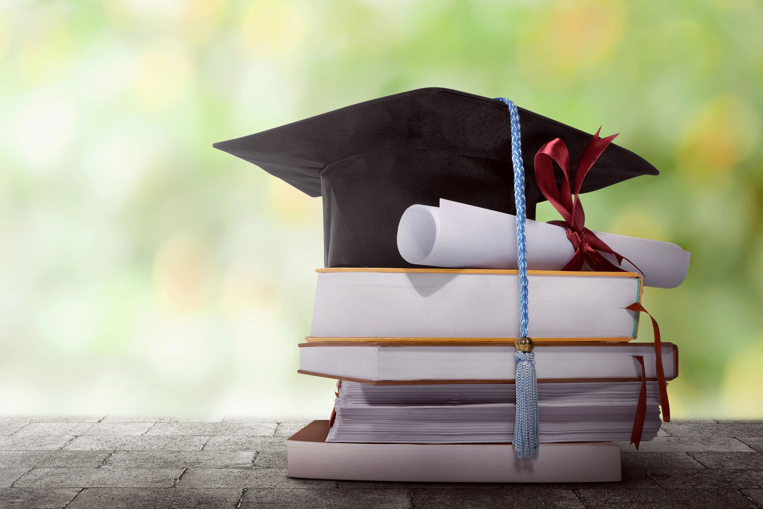 Graduation cap, diploma, and books stacked together.