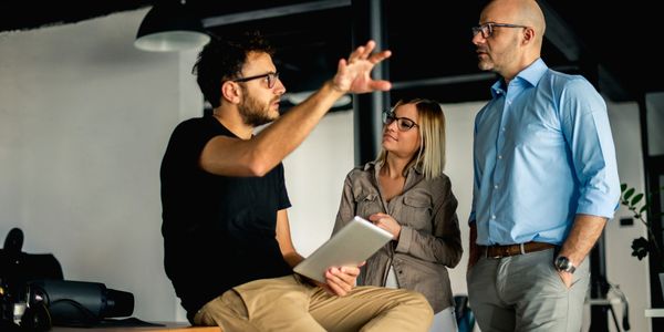 Three colleagues engaged in a discussion, one holding a tablet and gesturing.