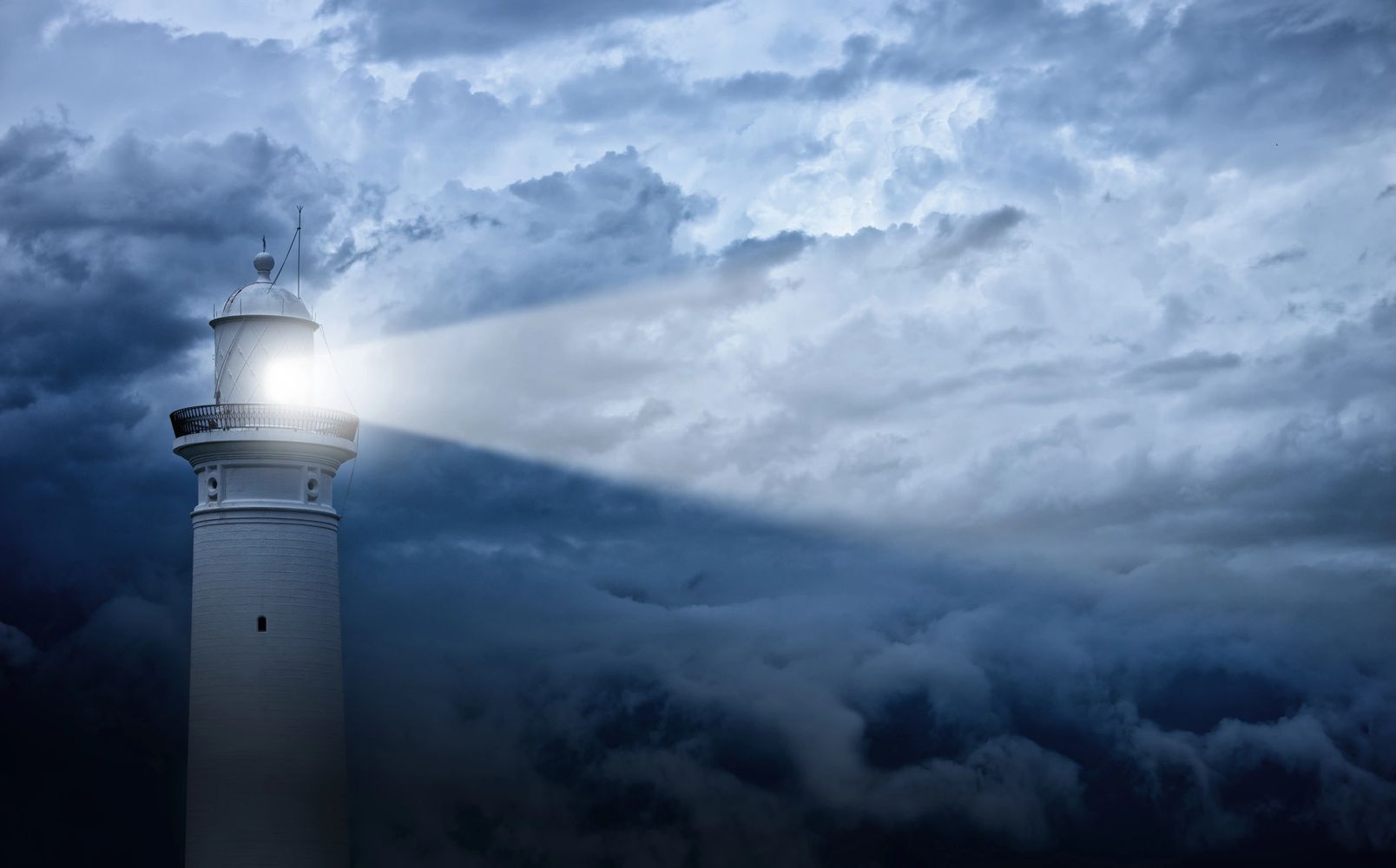 A lighthouse shining brightly through dark, stormy clouds at night.
