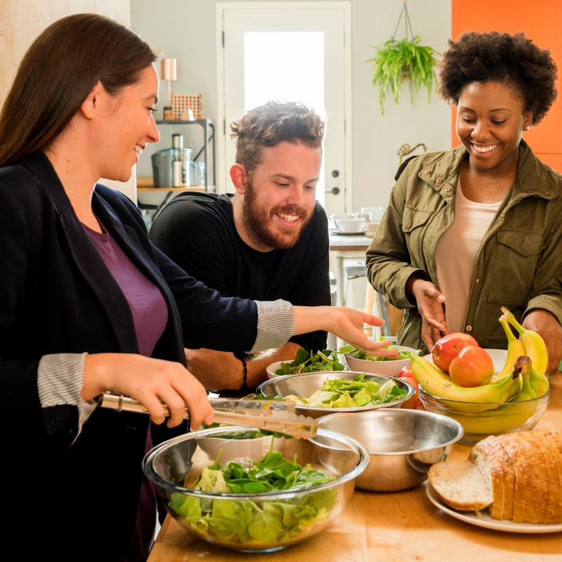 Friends preparing salad at home in the kitchen.