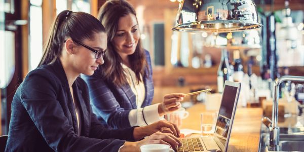 Two women working together on a laptop in a cozy cafe.