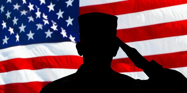 Silhouette of a soldier saluting in front of the American flag.