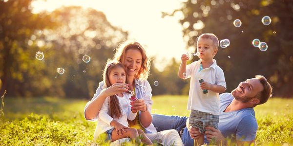A family enjoys blowing bubbles together in a sunny park.