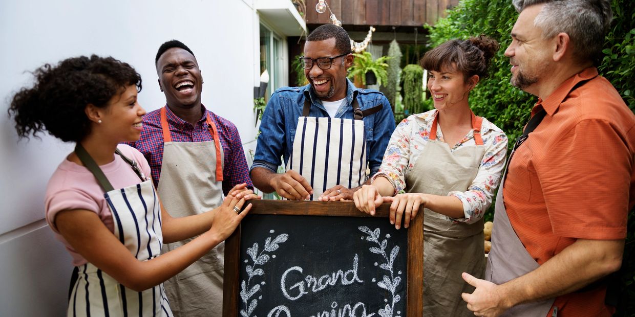 Happy team celebrating their grand opening with a chalkboard sign outdoors.