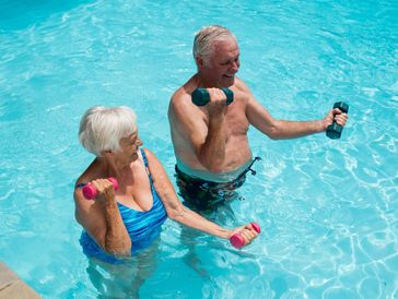 Elderly couple exercising with dumbbells in a swimming pool.