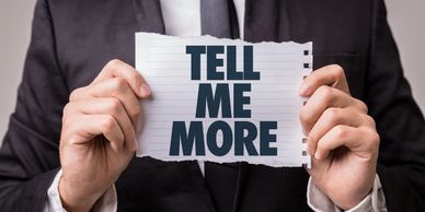 A man holding a paper saying "TELL ME MORE".