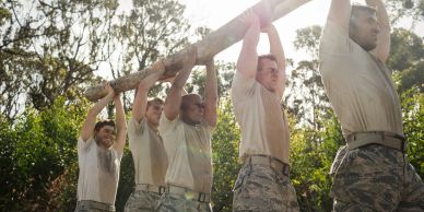 Soldiers lifting a heavy log together outdoors.