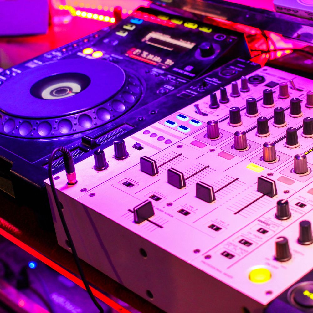 Close-up of a DJ mixer and turntable with vibrant purple lighting.