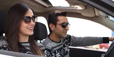 A smiling young couple wearing sunglasses driving a car.