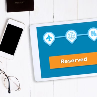 Tablet mostrando reserva de viaje junto a pasaporte, móvil y gafas.