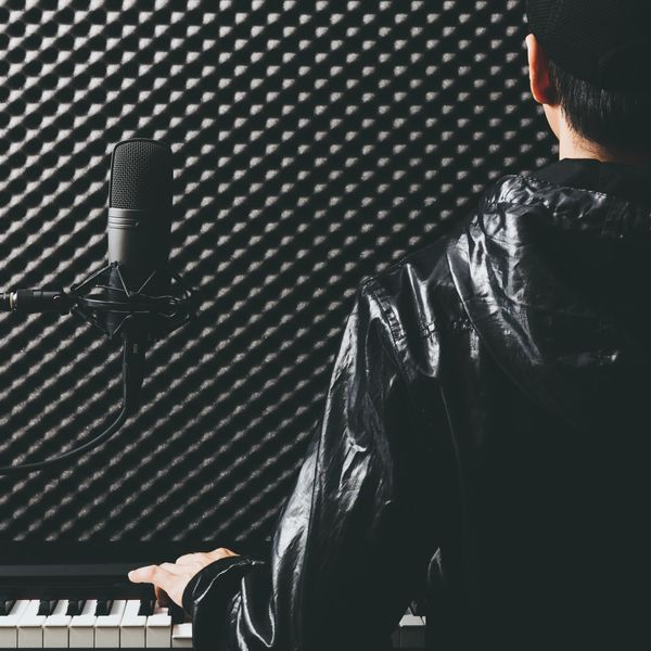 Musician in a soundproof studio playing piano and singing into a microphone.