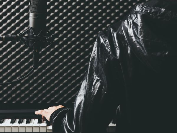 Musician in a soundproof studio playing piano and singing into a microphone.