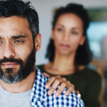 Depressed man with supportive hand on his shoulder from woman stood behind
