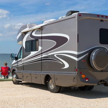 Recreational vehicle parked by a lake with a person sitting nearby.
