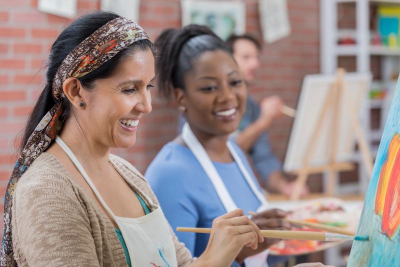 Cheerful Hispanic and African American friends enjoy painting together during art class.