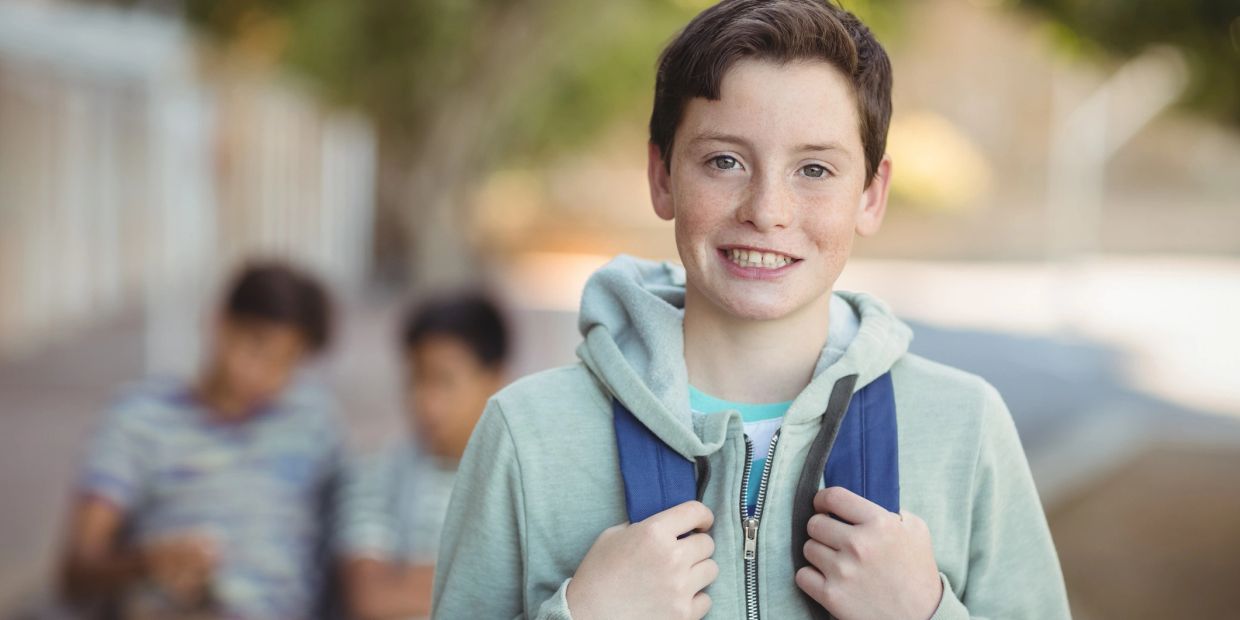 Smiling teenage boy with backpack outdoors.