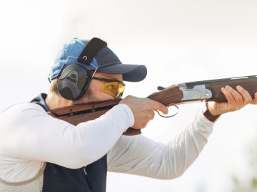 Man aiming shotgun while wearing protective gear.