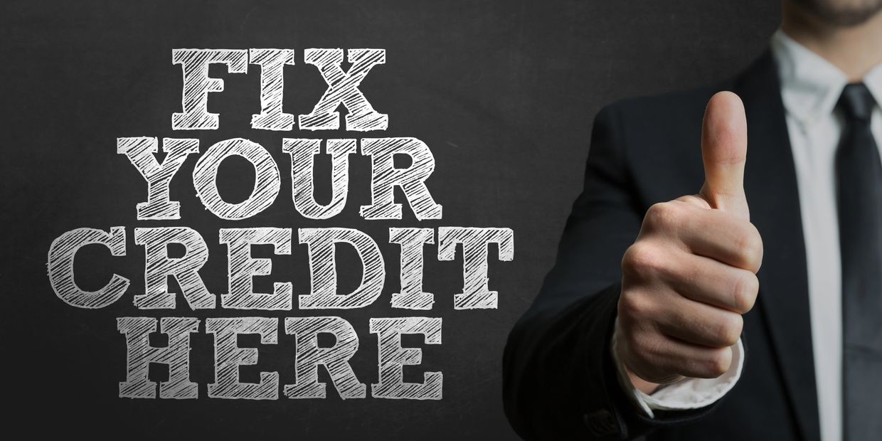 Businessman giving thumbs up next to 'Fix Your Credit Here' text on chalkboard.