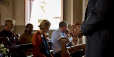 A person praying in a church with others seated.