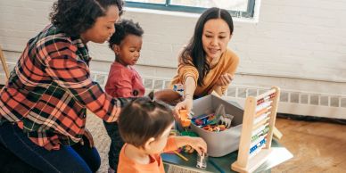 Two adults and two children playing with educational toys indoors.