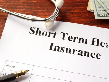 Short term health insurance form with a stethoscope and money on a wooden table.