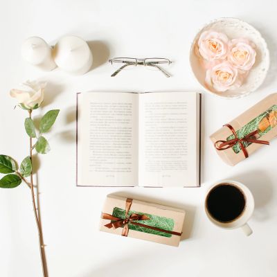 Open book with roses, coffee, candles, gifts, and glasses on a white table.