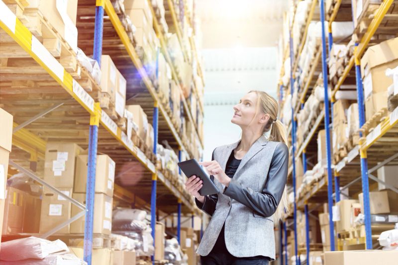Horizontal color image of woman working in warehouse on digital tablet. Planning, organization and preparation of deliveries.