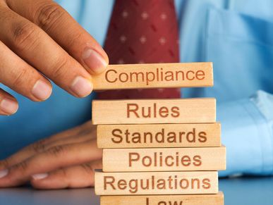 Hand placing a block labeled Compliance on top of other blocks representing rules and law.